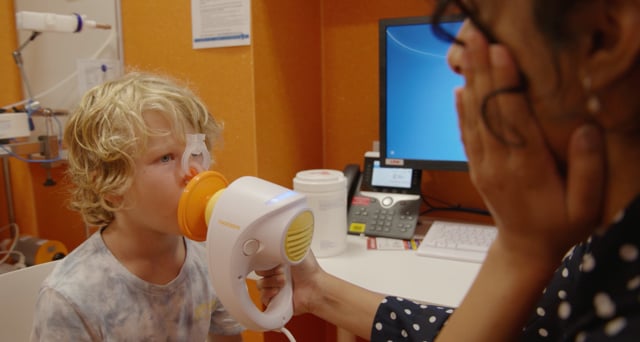 Little boy with lung function test mask over face with a researcher.